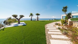Une pelouse bien entretenue, avec un chemin de pierres menant à un bâtiment moderne doté de grandes fenêtres et offrant une vue sur la mer.