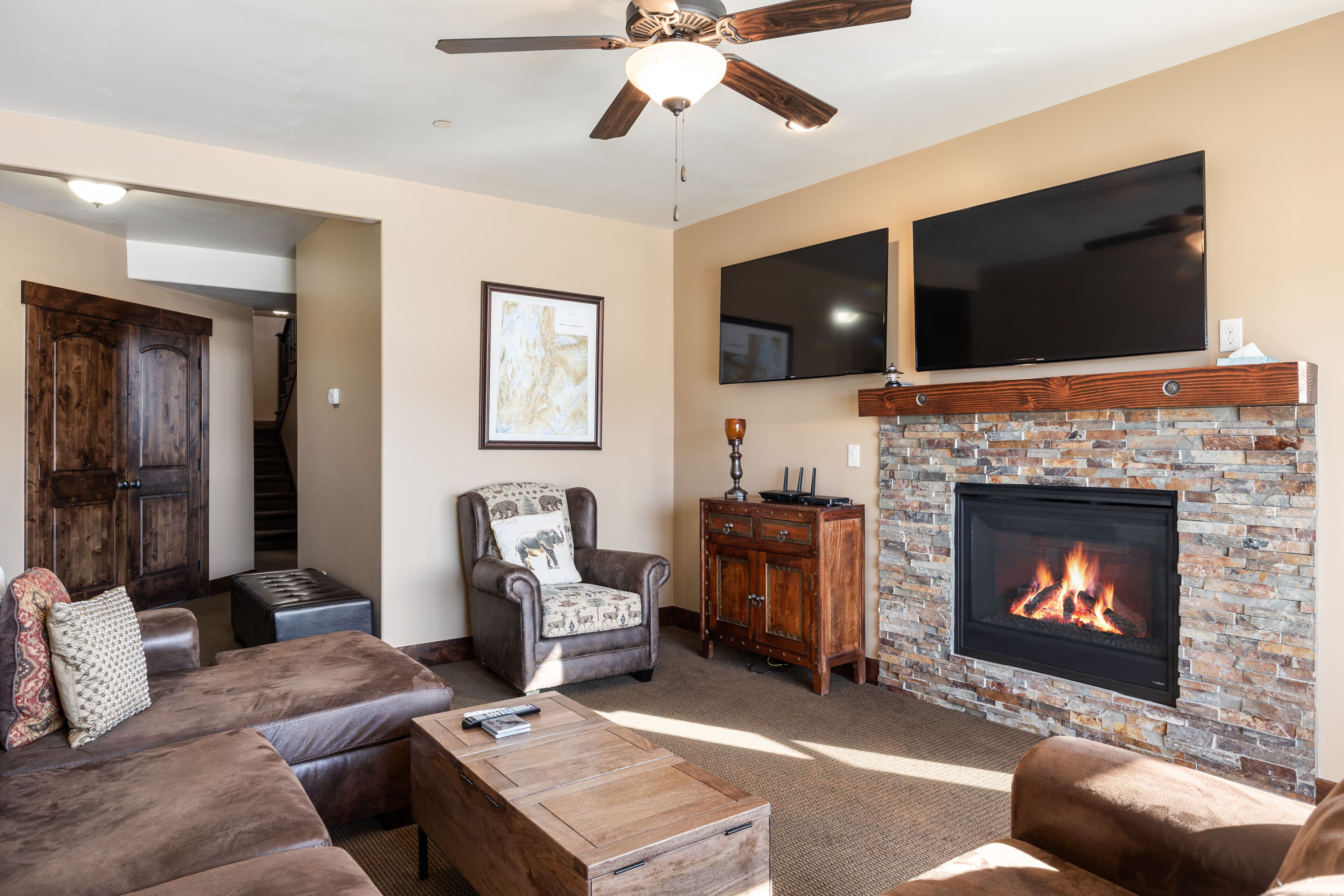 A living room with a fireplace, leather furniture, a ceiling fan, and a TV mounted above the fireplace.