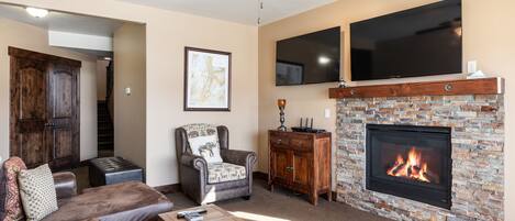 A living room with a fireplace, leather furniture, a ceiling fan, and a TV mounted above the fireplace.