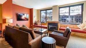 A cozy living room with a fireplace, a large TV, and a view of a snowy mountain. - Grand Summit Hotel | Great Ski Location! Luxury and Comfort (Park City)