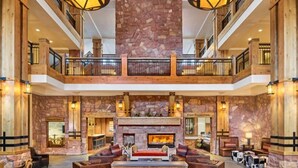 A spacious lobby with a stone fireplace, wooden furniture, and a second-floor balcony. - The Grand Summit Hotel in the Canyons Village - Close to Golf - Pool, Gym, Spa, More! (Park City)