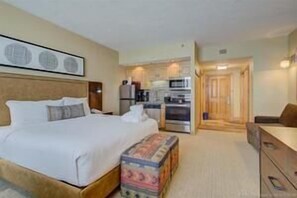 Una habitación de hotel con una cama, un escritorio pequeño, una kitchenette y una puerta que da a otra habitación.