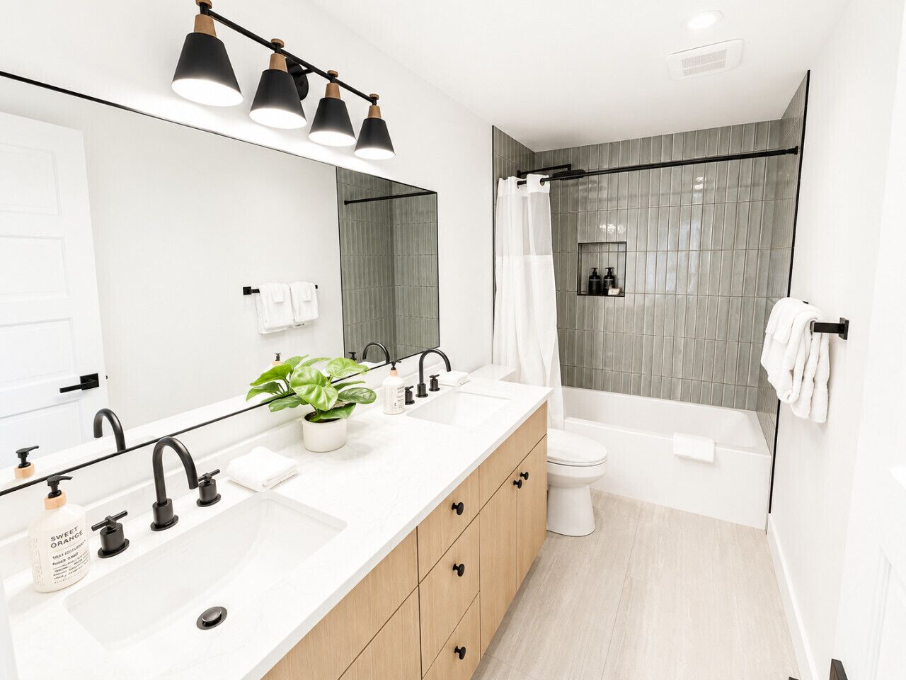 Un baño moderno con tocador doble lavamanos, ducha con puerta de vidrio y un espejo grande.