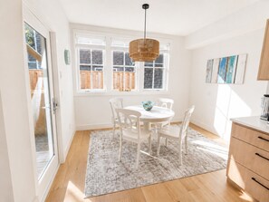 Une cuisine moderne avec une table à manger ronde, des chaises blanches, un plancher en bois et une grande fenêtre avec des stores.