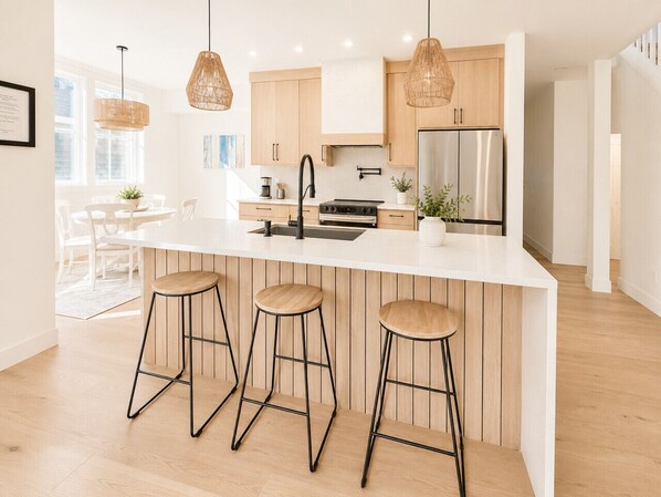 A modern kitchen with a white island, wooden bar stools, and pendant lighting.