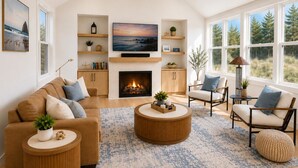 A living room with a fireplace, a television, and a large window with a view of trees. - Luxury Beach Home | 1-Min Walk to Sand | 4BR/4BA | Best Location in Shorepine Village (Pacific city)