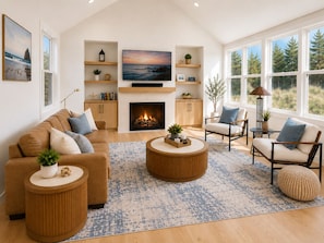 A living room with a fireplace, a television, and a large window with a view of trees.