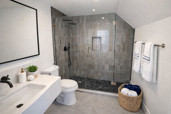 A modern bathroom with a glass-enclosed shower, a white toilet, and a large mirror.