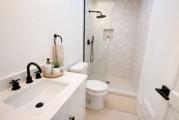 A bathroom with a white sink, black faucet, toilet, and a glass-enclosed shower area.