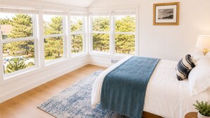 A bedroom with a large window, a bed with a blue blanket, a wooden floor, and a framed picture on the wall. - Luxury Beach Home | 1-Min Walk to Sand | 4BR/4BA | Best Location in Shorepine Village (Pacific city)