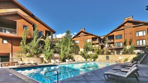A hotel with a swimming pool, lounge chairs, and a stone wall.