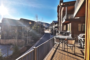 A wooden deck with outdoor furniture, a barbecue grill, and a view of a mountain.