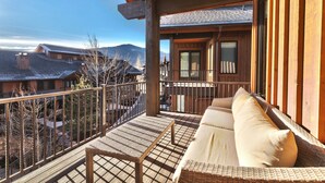 A balcony with a wicker sofa and a table, overlooking a mountainous landscape.