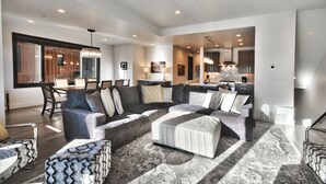 A spacious living room with a large sectional sofa, a patterned ottoman, and a dining area with chairs.