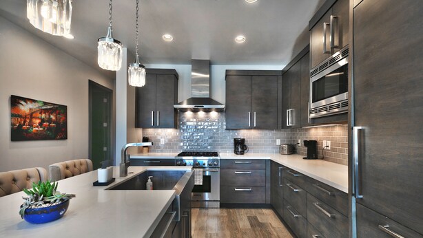 A modern kitchen with dark cabinetry, stainless steel appliances, a large island, and pendant lighting.