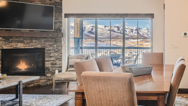 A modern living room with a fireplace, a large flat-screen TV, and a dining area with a view of mountains. - Private Hot Tub, Close to Resorts - Private Hot Tub - Close to PC, Mountain Mansion Family Getaway (Heber City)