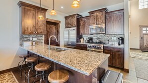 A kitchen with granite countertops, wooden cabinets, stainless steel appliances, and bar stools. - Private Hot Tub, Close to Resorts - Private Hot Tub - Close to PC, Mountain Mansion Family Getaway (Heber City)