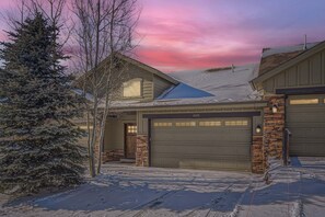 A residential house with a garage, a snow-covered driveway, and a large evergreen tree. - Private Hot Tub, Close to Resorts - Private Hot Tub - Close to PC, Mountain Mansion Family Getaway (Heber City)