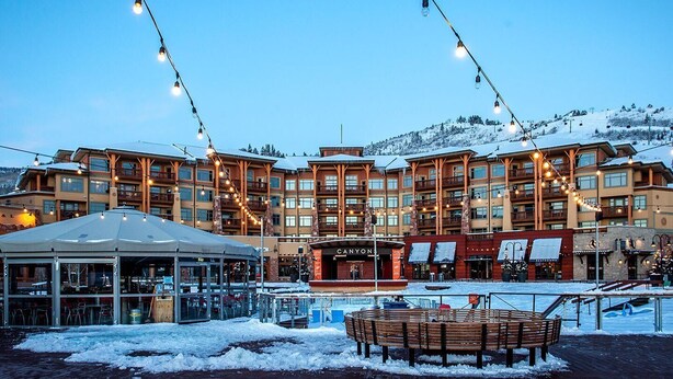 A multi-story hotel with a snow-covered ground, outdoor seating area, and string lights.