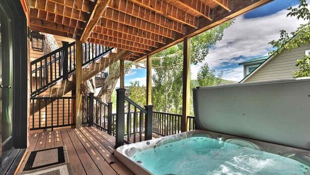 A wooden deck with a hot tub, wooden stairs, and a view of trees and a house. - Beautiful Historic Town Home, Walk to Main St - Large Deck w/ Mountain Views and Private Hot Tub! (Park City)