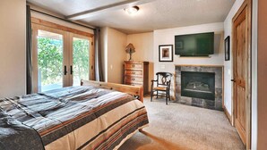 A bedroom with a bed, dresser, chair, fireplace, and TV. - Beautiful Historic Town Home, Walk to Main St - Large Deck w/ Mountain Views and Private Hot Tub! (Park City)