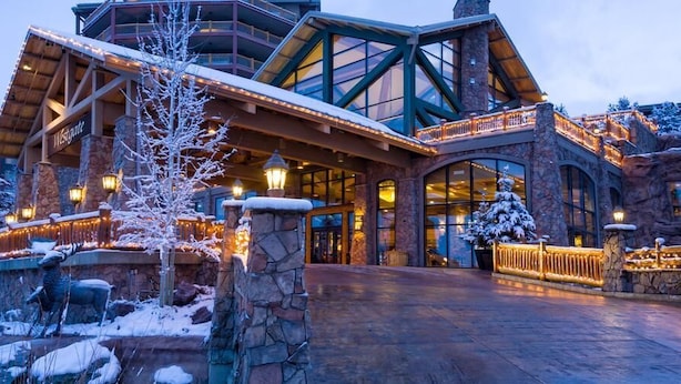Un grand chalet de style rustique, doté d’une façade en pierre, de grandes fenêtres et d’un espace d’entrée abrité.