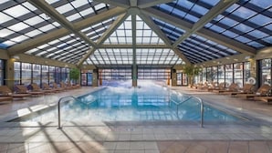 Une piscine intérieure dotée d’un toit en verre, de chaises longues et offrant une vue sur l’extérieur.
