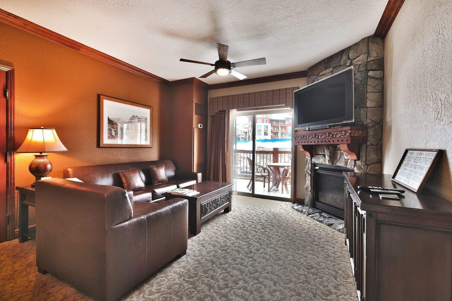 Habitación de hotel con sofá de cuero, televisor de pantalla plana, chimenea y balcón con vistas a edificios.