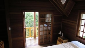 A wooden room with a bed, a nightstand, a window, and a door leading to an outdoor balcony. - Pousada Floresta Negra (Canela)