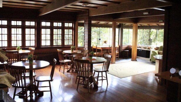 A spacious dining area with wooden tables and chairs, large windows, and a view of the outdoors. - Pousada Floresta Negra (Canela)