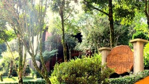 A lush garden with a large, rustic stone sign. - Pousada Floresta Negra (Canela)