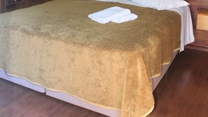 A neatly made bed with a brown bedspread, white pillows, and a white canopy. There is a wooden wardrobe with folded towels and a hanging rack. - Pousada Floresta Negra (Canela)