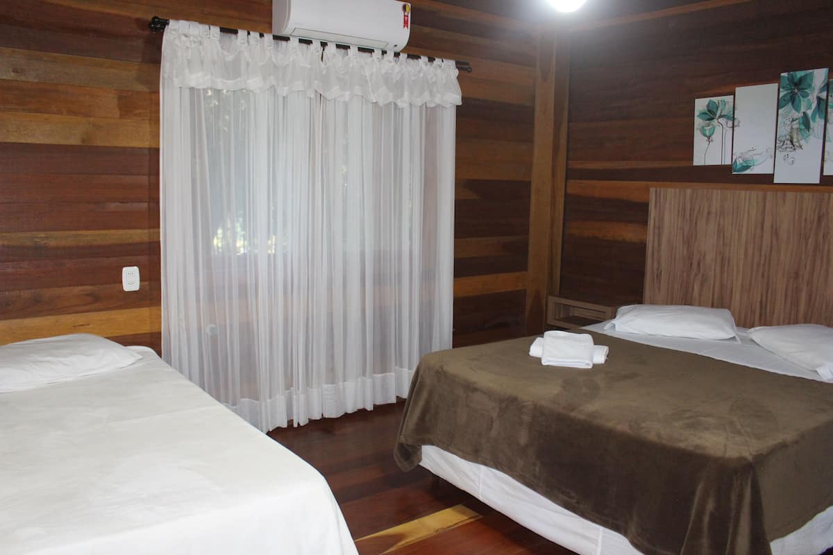 Una habitación con dos camas, una pared de madera, una cortina blanca y un aire acondicionado instalado en la pared.