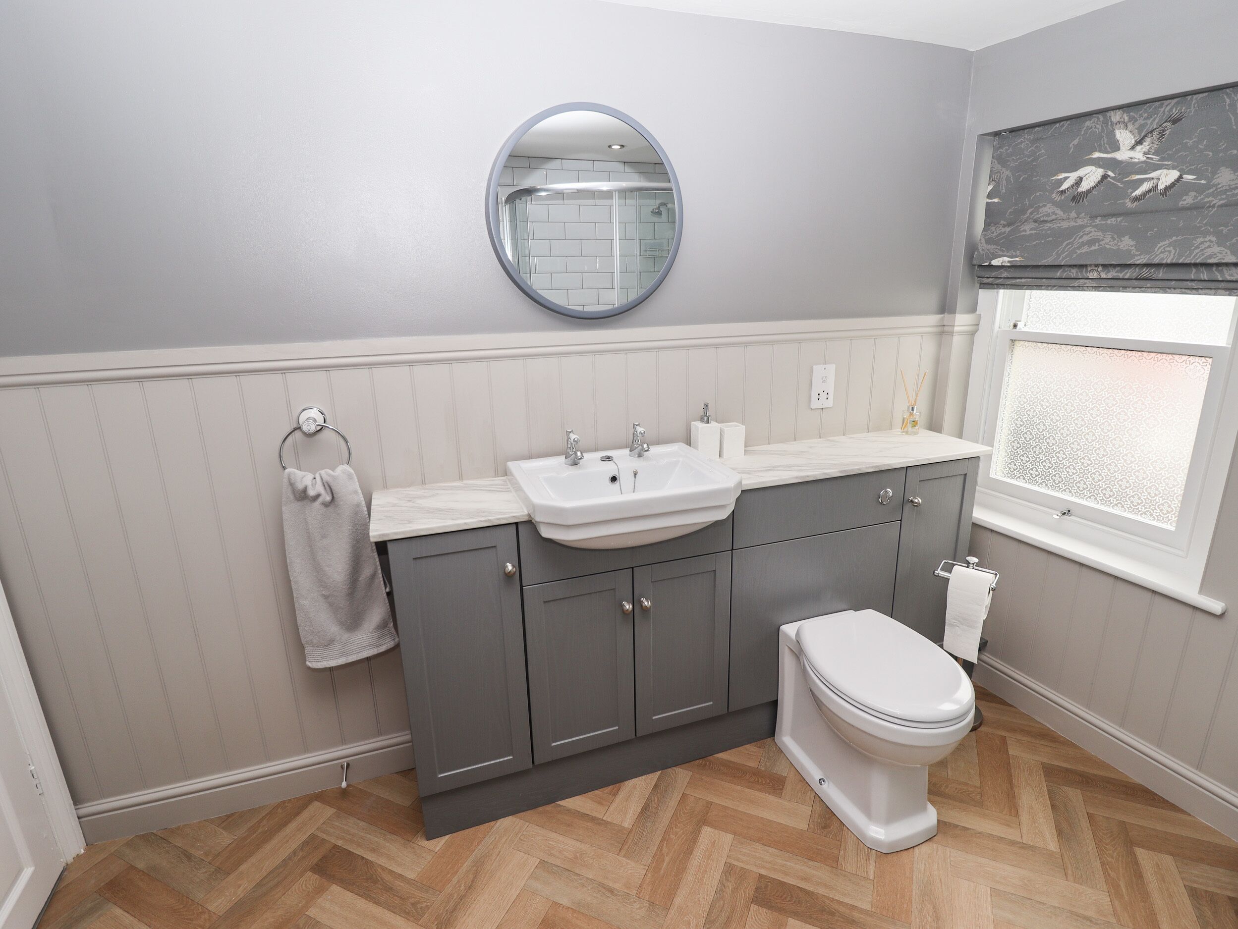 A bathroom with a sink, mirror, toilet, and a window with a view of birds.