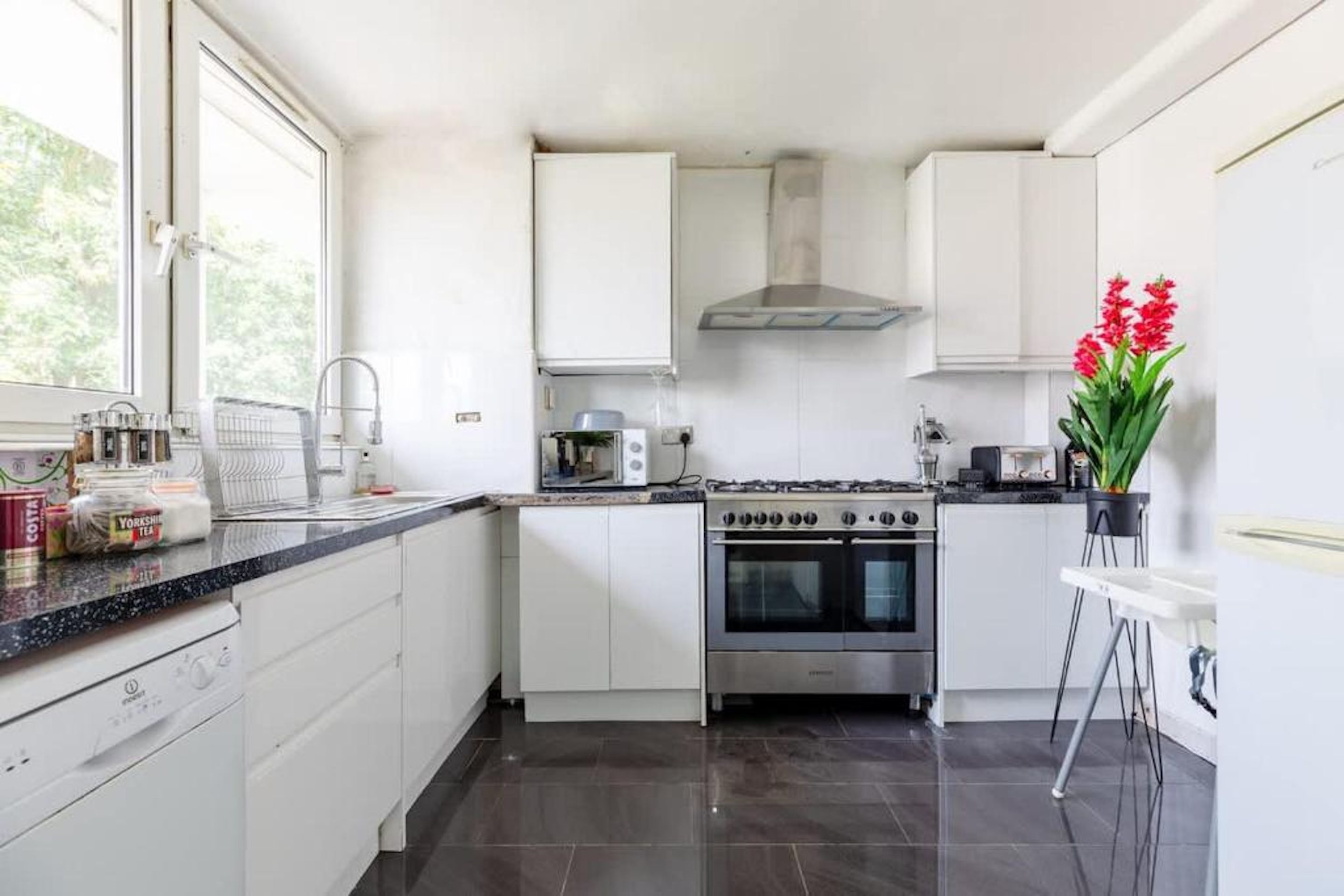 Une cuisine moderne avec des meubles blancs, une cuisinière en acier inoxydable et une fenêtre qui laisse entrer la lumière naturelle.