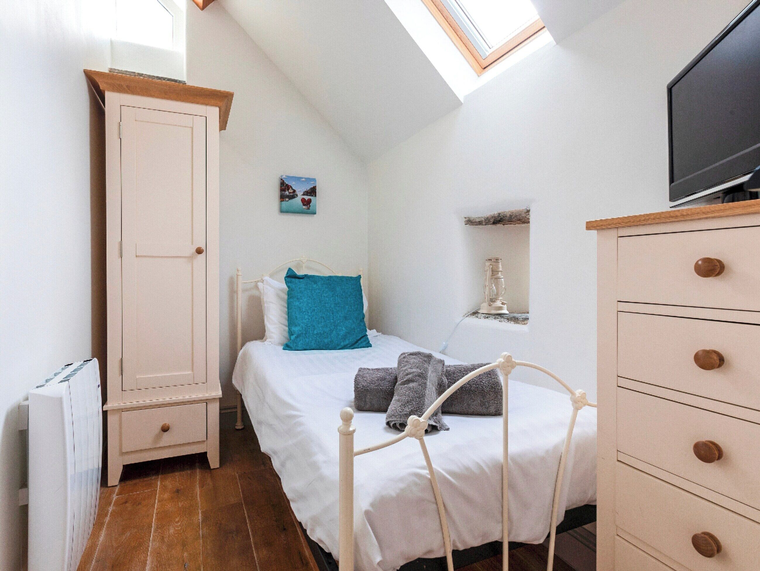A bedroom with a bed, a wardrobe, a small shelf with a lamp, and a television on a dresser.