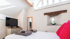 A bedroom with a bed, a television on a dresser, a mirror, and a shelf with decorative items. - 3 bedroom accommodation in Stoke Fleming, near Dartmouth (Stoke Fleming, near Dartmouth)