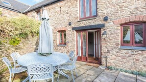 A stone building with a patio area featuring a round table and chairs, a covered umbrella, and a door with glass panels. - 3 bedroom accommodation in Stoke Fleming, near Dartmouth (Stoke Fleming, near Dartmouth)