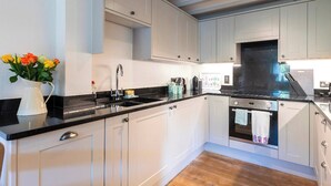 A modern kitchen with white cabinets, a black countertop, and a wooden floor. - 3 bedroom accommodation in Stoke Fleming, near Dartmouth (Stoke Fleming, near Dartmouth)