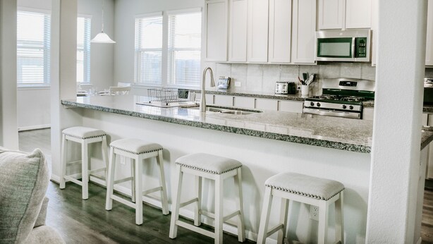 A modern kitchen with white cabinets, a granite countertop, a stainless steel stove, and bar stools.