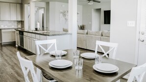 A modern kitchen with white cabinets, a wooden dining table set for four, and a large island with a sink.