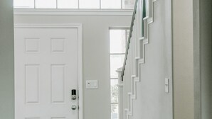 A hallway with a white door, a staircase with a white railing, and a hanging light fixture.