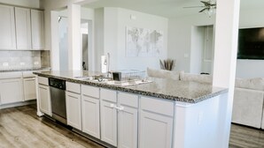 A modern kitchen with white cabinetry, a granite countertop, and a built-in dishwasher.