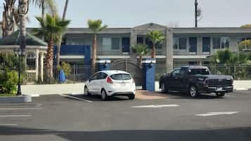 A parking lot with a white car and a black truck, a building with a blue facade, and palm trees.