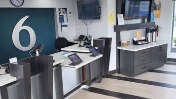 A reception area with a large number '6' on the wall, a clock, a flat-screen TV, and a counter with a laptop.