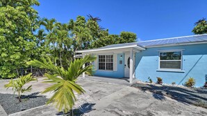 A residential house with a blue exterior, a front porch, and a small garden with palm trees.
