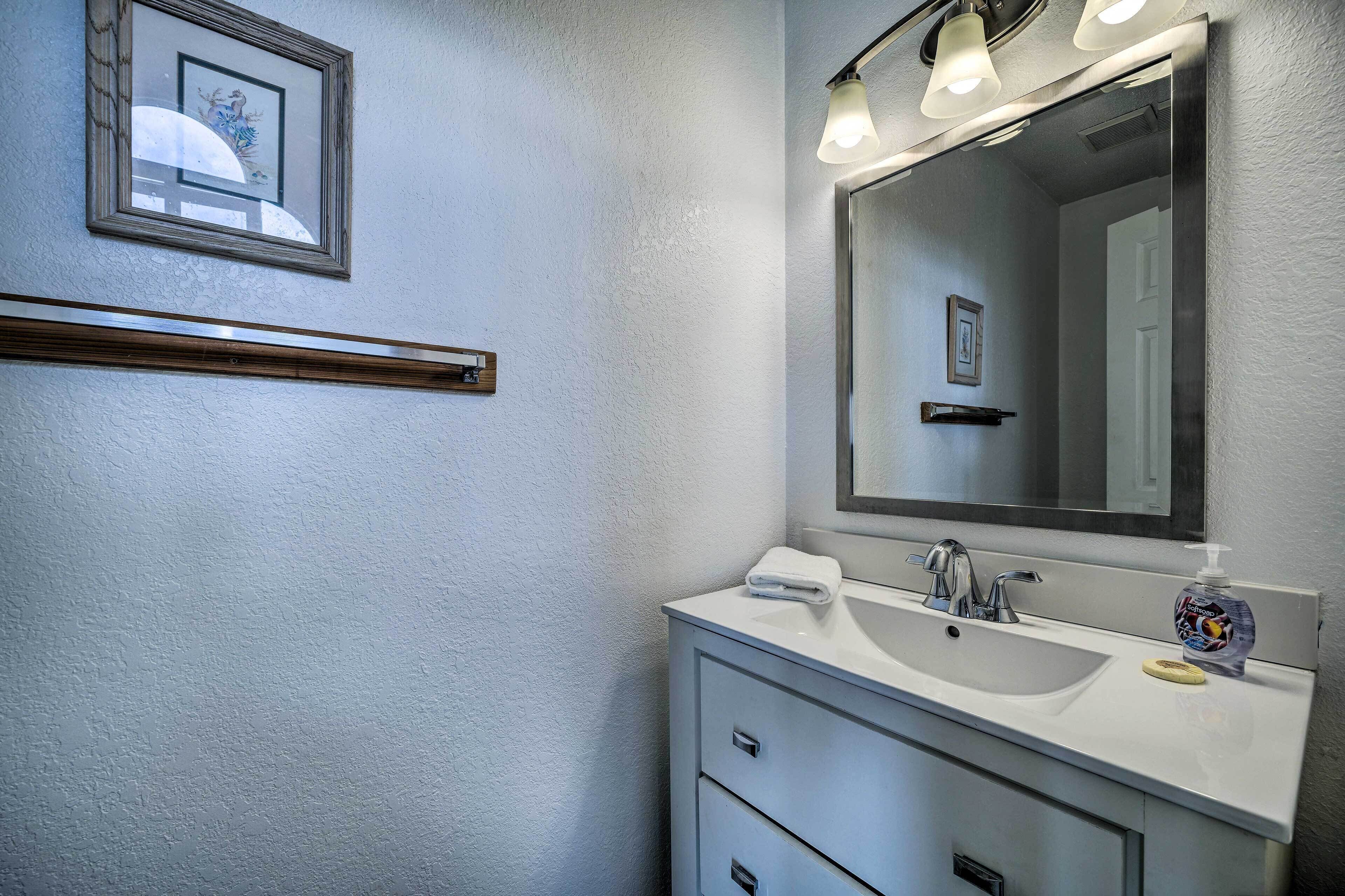 A bathroom with a white sink, a mirror, and a framed picture on the wall.
