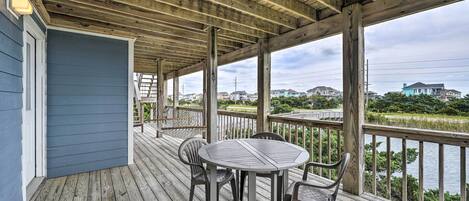 A covered deck with a table and chairs, overlooking a body of water and houses.