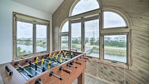 Ein Kicker-Tisch in einem Raum mit großen Bogenfenstern mit Blick auf ein Gewässer und Gebäude.