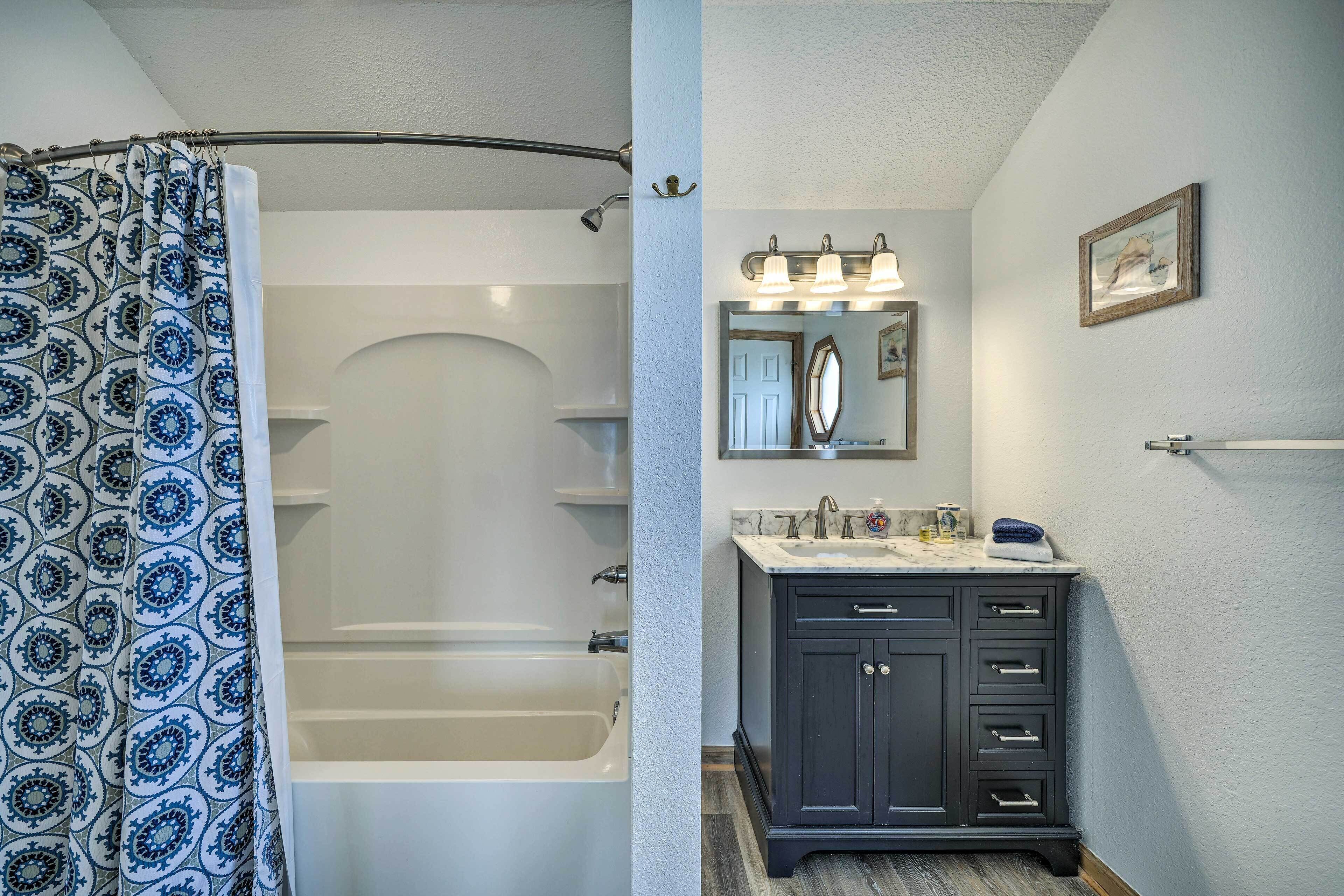 A bathroom with a bathtub, a vanity with a mirror, and a shower curtain.